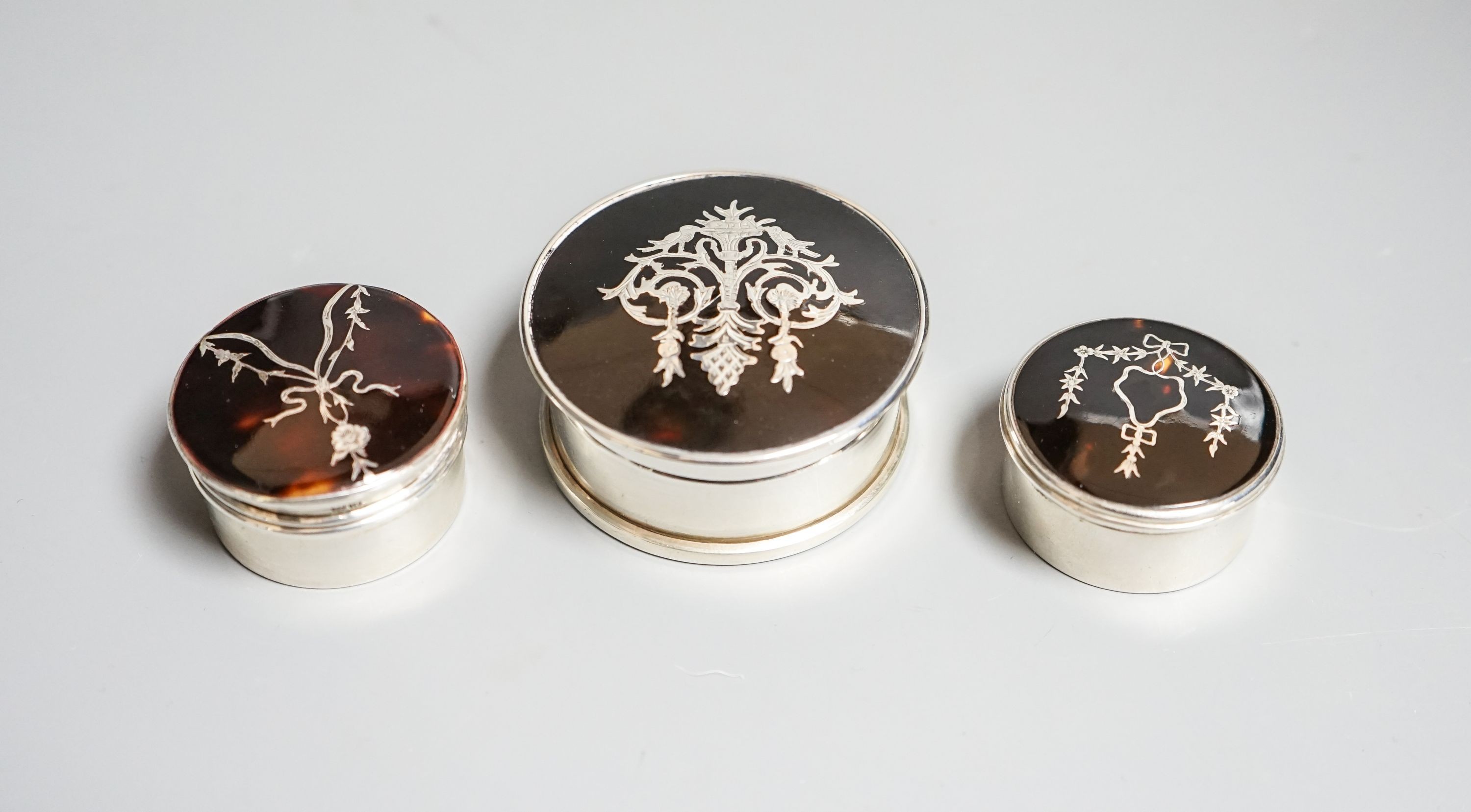 Three assorted early 20th century silver and tortoiseshell pique circular boxes and covers, including William Comyns, largest 63mm.